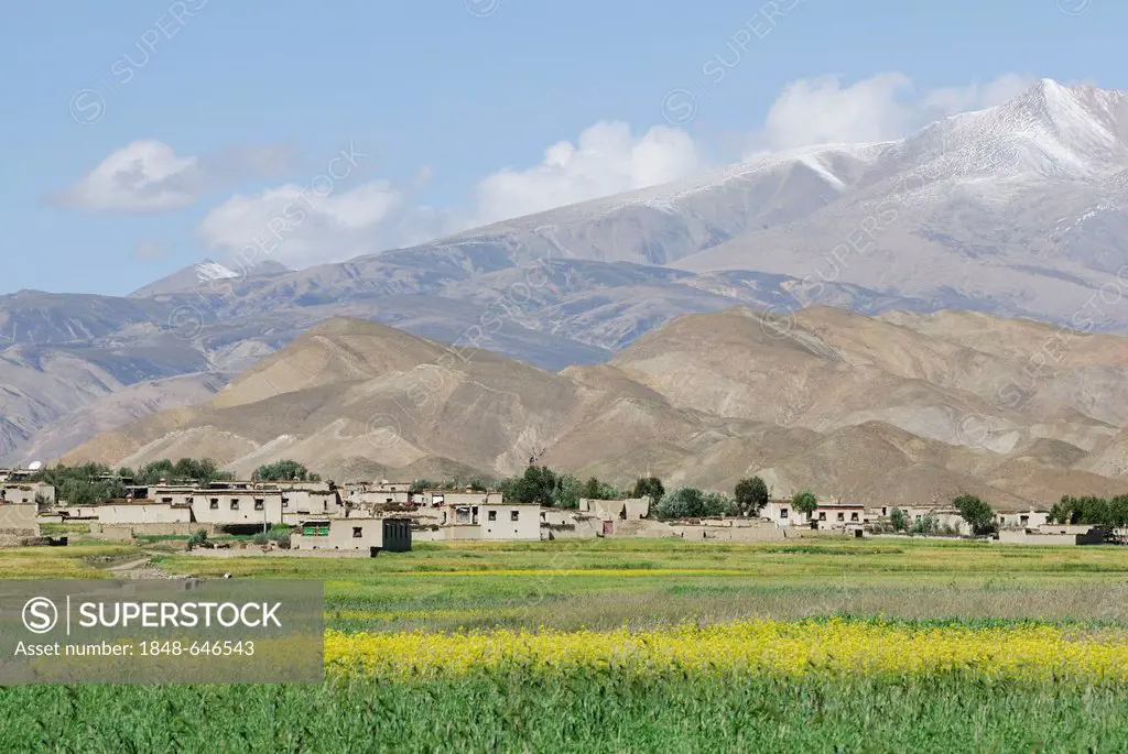 Fields and a Tibetan village in front of a mountain landscape, Friendship Highway between Shigatse and Lhatse, Tibet, China, Asia