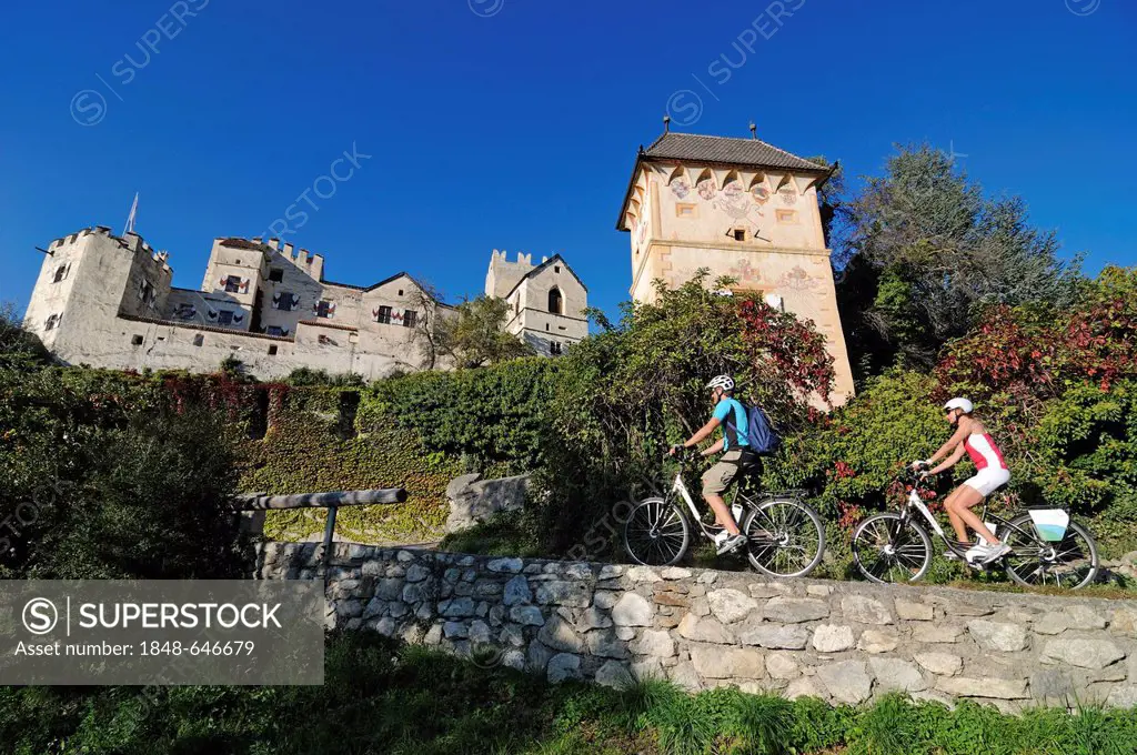 Couple riding electric bicycles past Kastelbell castle, Tschars, province of Bolzano-Bozen, Italy, Europe