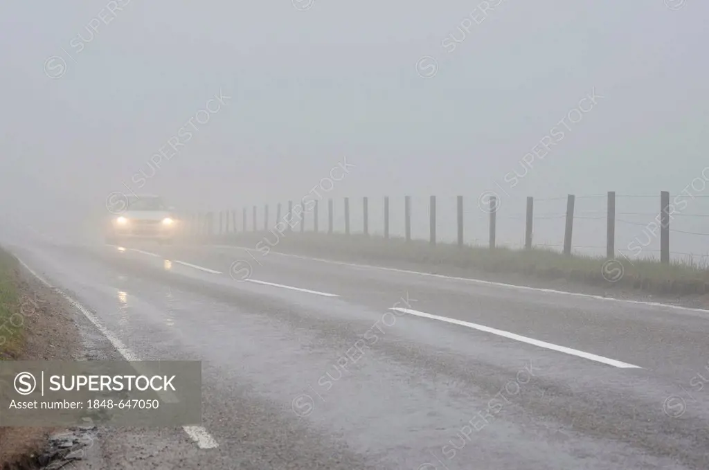 Car travelling with headlights on in dense fog on a road in the Scottish Highlands, Grampian Mountains, Scotland, United Kingdom, Europe