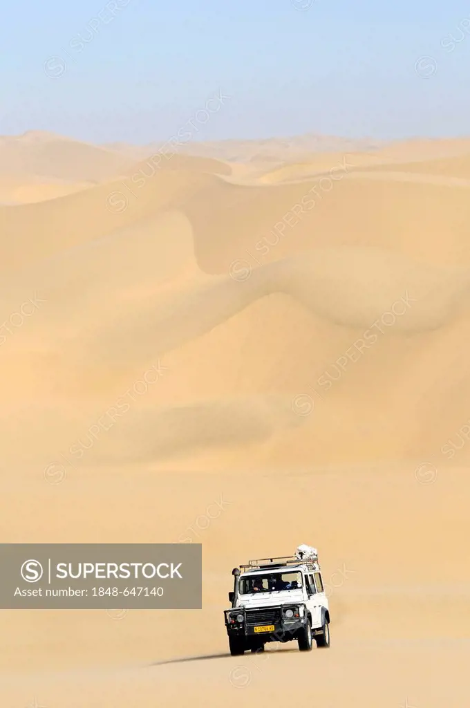 Landrover Defender off-road vehicle driving through sand dunes, Namib Naukluft National Park, part of the Namibian Skeleton Coast National Park, Skele...
