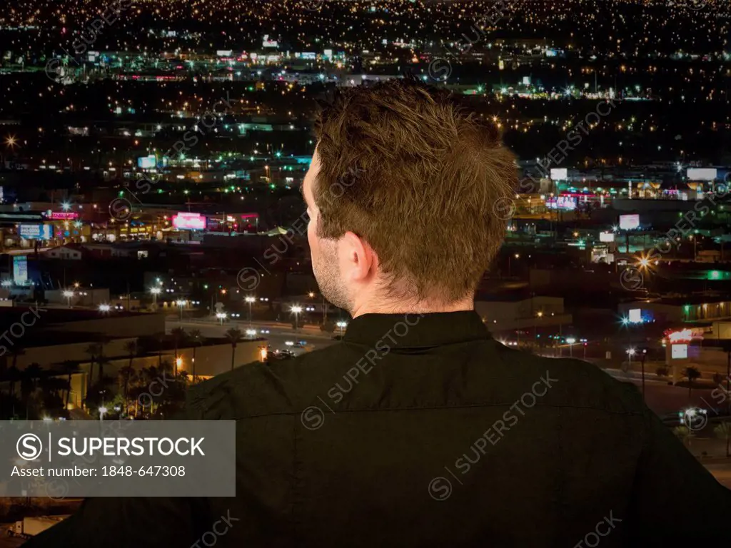 Businessman looking onto an illuminated city at night, seen from behind