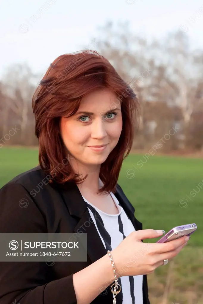 Smiling young woman, 25, holding an iPhone in her hand