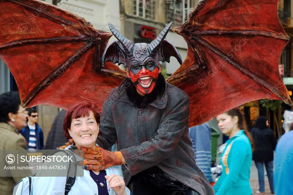 Man wearing a Lucifer costume strangling a smiling woman, crude carnival characters and satirical sculptures at a parade, Fallas festival, Falles fest...