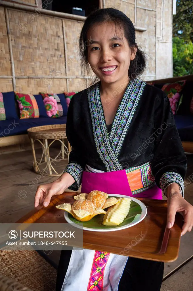 Traditionally dressed smiling waitress serving a fruit plate, woman from the Black Hmong hill tribe, ethnic minority from East Asia, Northern Thailand...