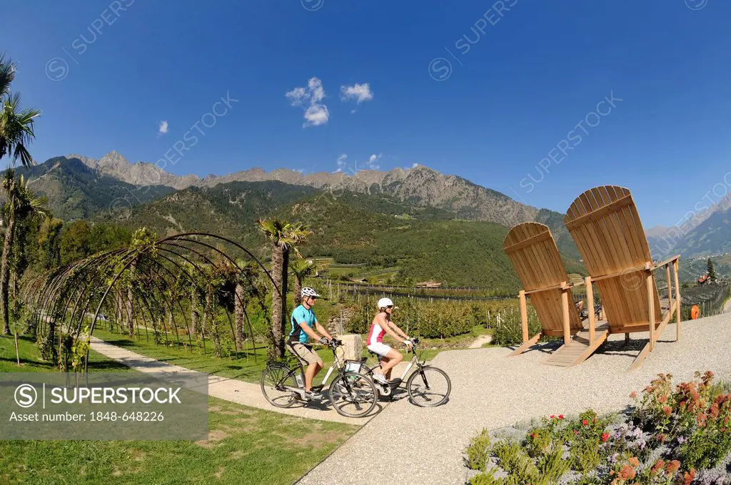Giant chairs, view of Merano as seen from Algund, couple riding electric bicycles, province of Bolzano-Bozen, Italy, Europe