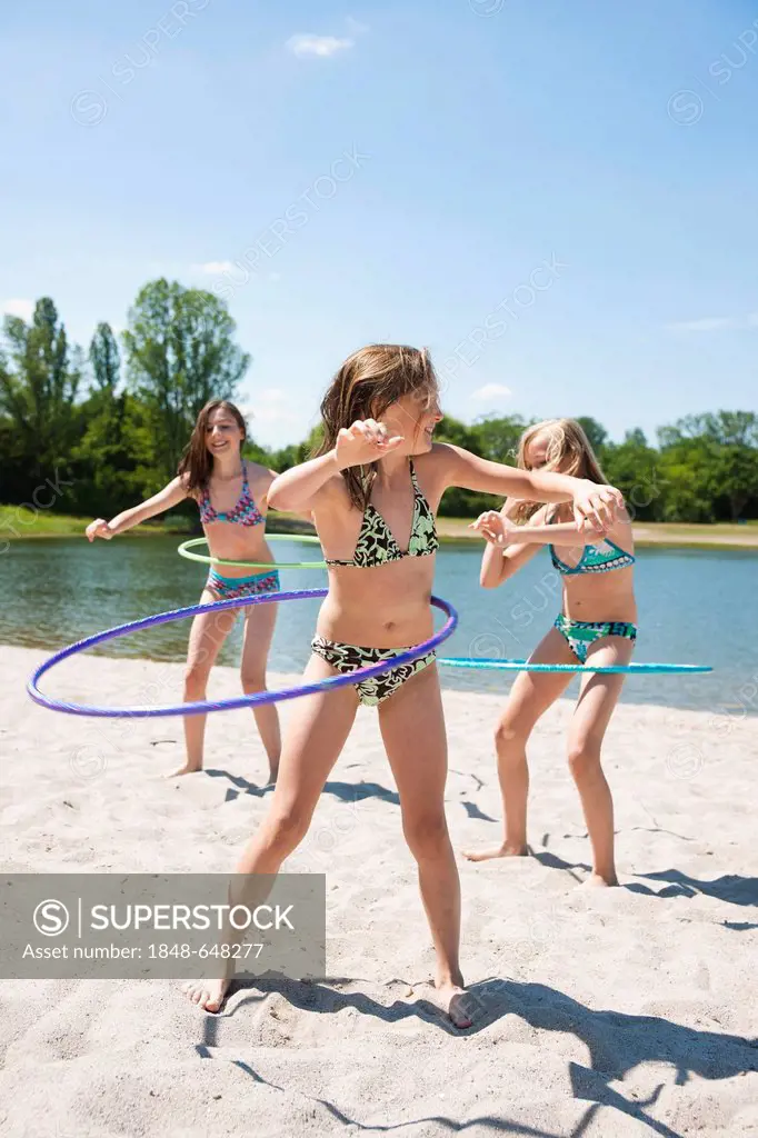 Girls playing with hula-hoops on the beach of a lake