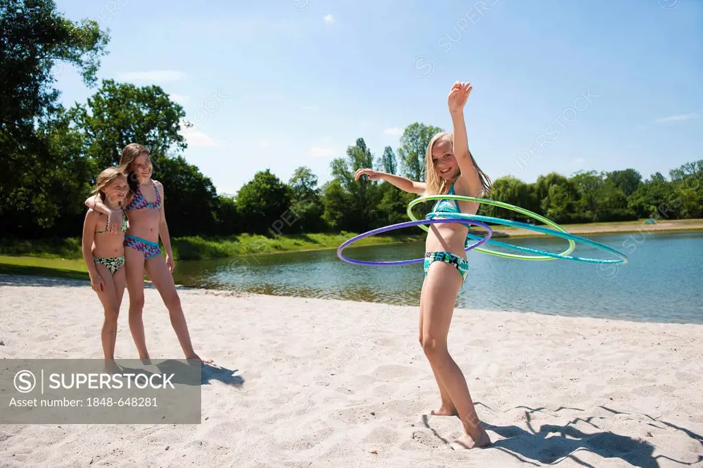 Girls playing with hula-hoops on the beach of a lake