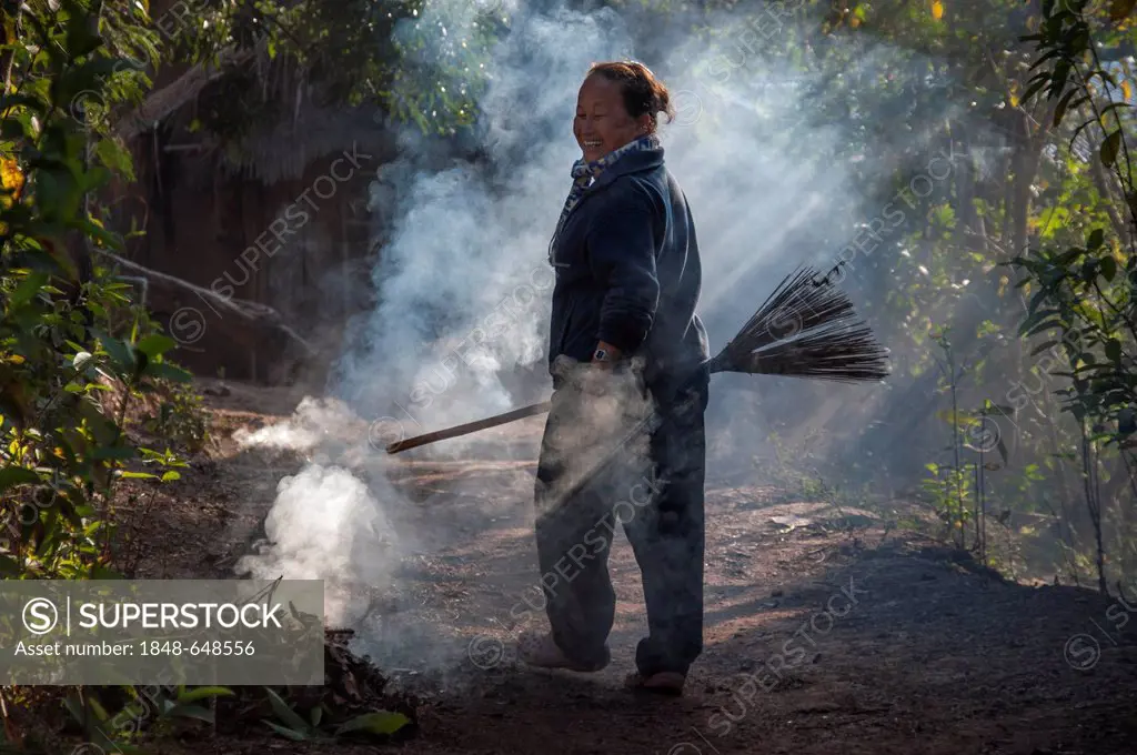 Smiling woman with a broom, smoke, waste incineration, village of hill tribe people, Hmong people, an ethnic minority, northern Thailand, Thailand, As...