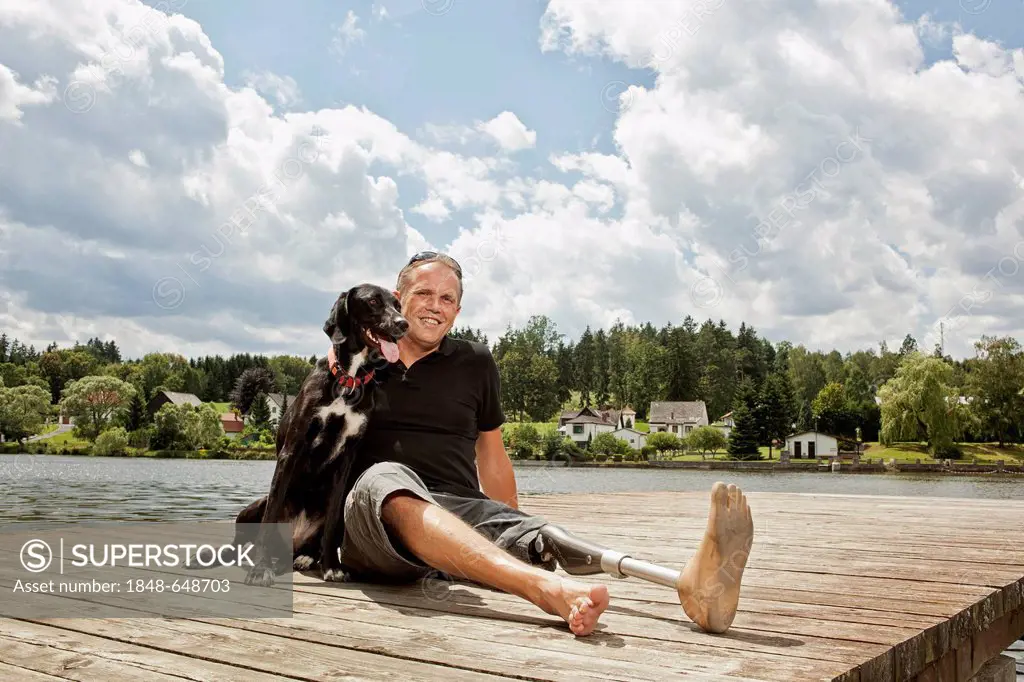 Man with a prosthetic leg sitting on a jetty with his hunting dog