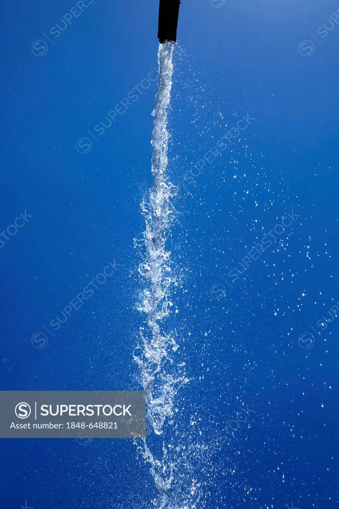 A jet of water flowing from a high-level fountain in front of the blue sky, in the gardens of the Moorish King's Palace of Real Alcazar, Seville, Anda...