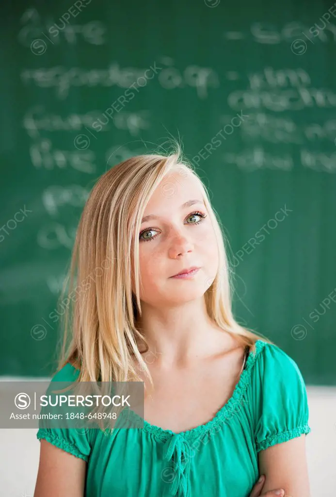 Schoolgirl standing in front of a blackboard in a classroom, portrait