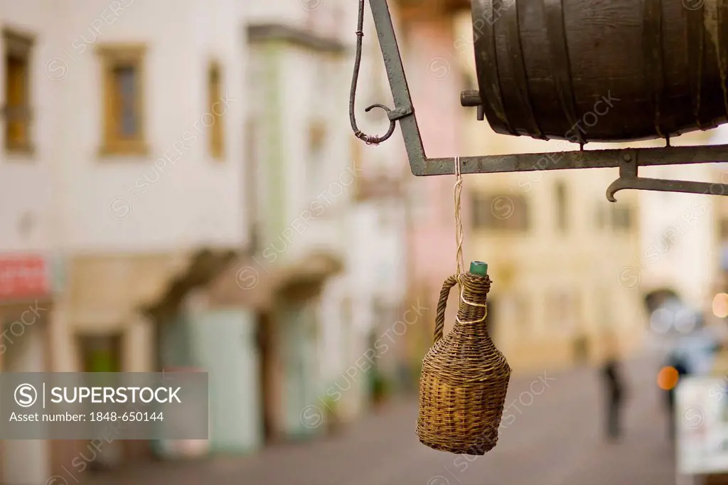 Wicker wrapped wine bottle hanging in front of a store, Caldaro, Alto Adige, Italy, Europe
