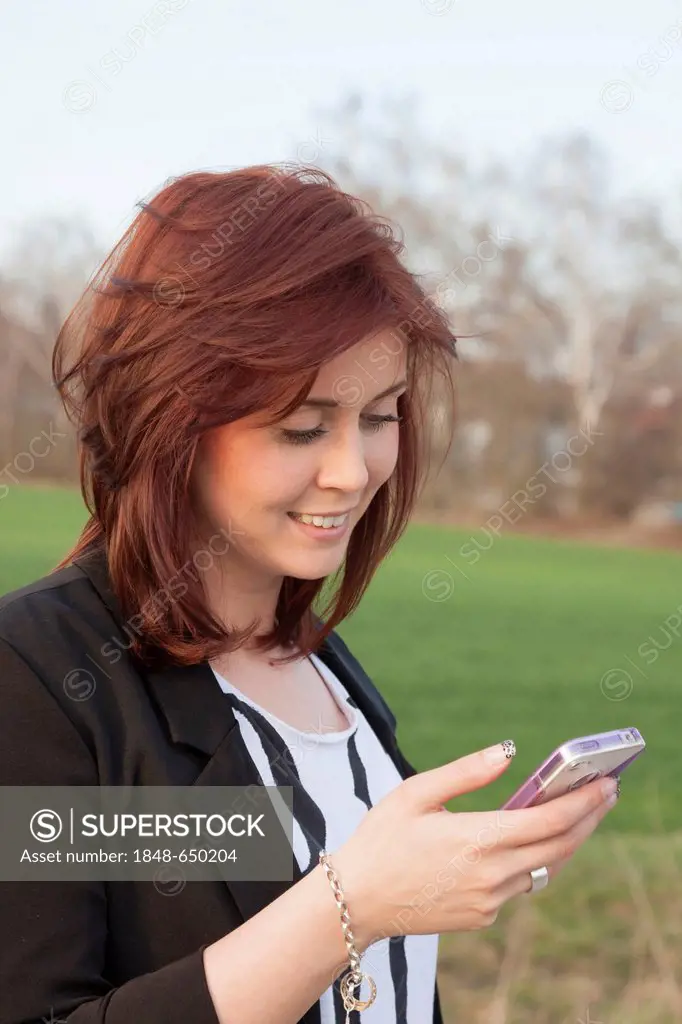 Young woman, 25, smiling while reading a text message on an iPhone
