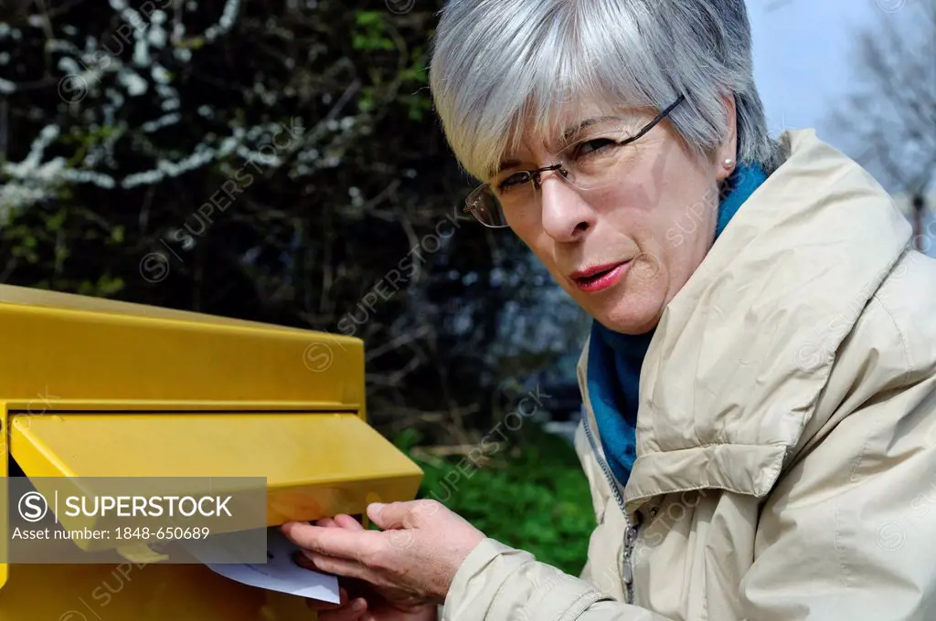 Woman putting a letter into a mailbox, Germany, Europe