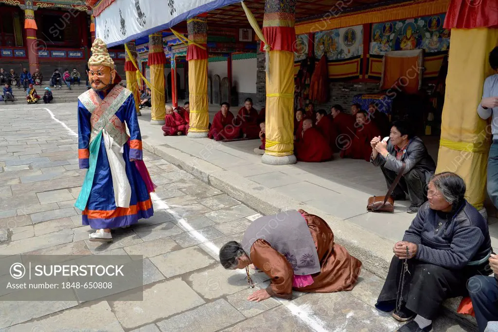 Tibetan Buddhism, woman kneeling in prayer to the religious masked Cham dance, at the important Kumbum Monastery, Gelug or Gelug-pa yellow hat sect, T...