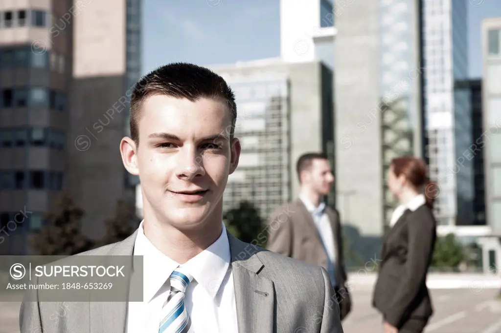 Businessman, portrait, two colleagues at back, tall buildings