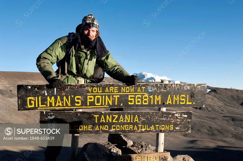 Trekking, mountain climber standing at the sign at the summit of Gilman's Point, stepped glacier on the crater rim, Kilimanjaro, Marangu Route, Tanzan...