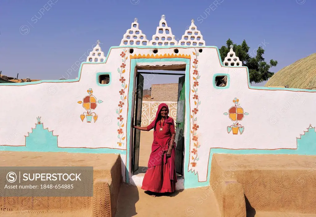Traditional painted house in the Thar desert, an Indian woman in a red sari in the entrance, Thar Desert, Rajasthan, India, Asia