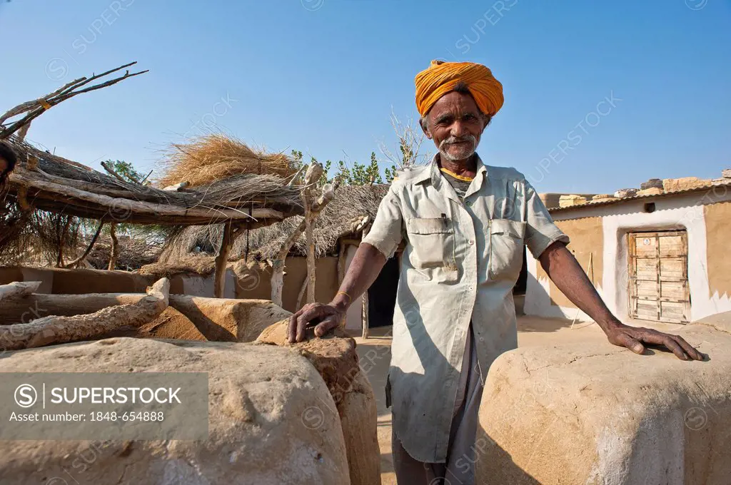 A friendly elderly man wearing a turban standing next to his property's wall, Thar Desert, Rajasthan, India, Asia