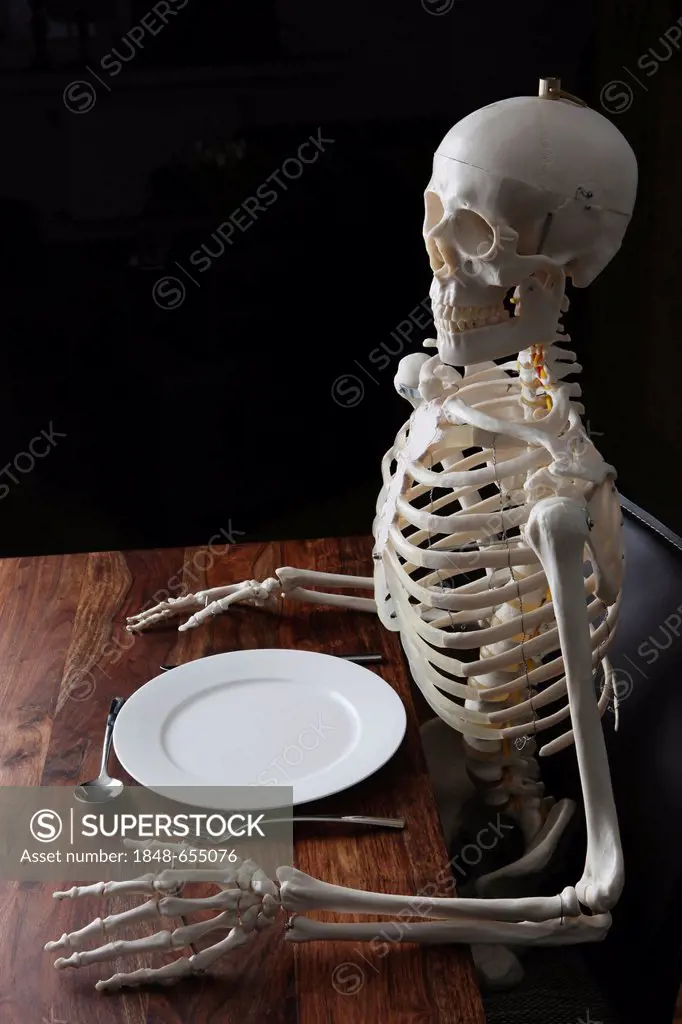 Skeleton sitting at a laid table with a plate, a knife, a spoon and a fork