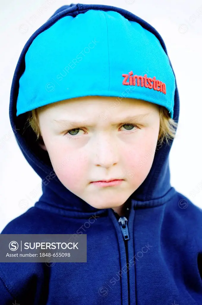 Grim faced 5-year-old boy wearing a baseball cap and a hoodie jacket, portrait