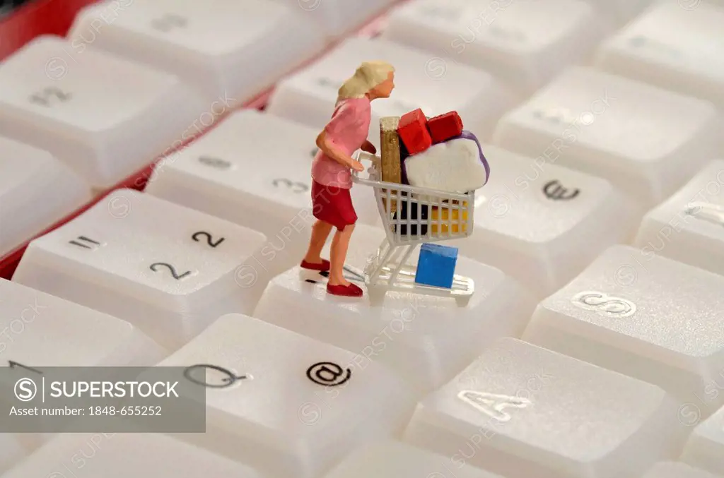 Woman with an overflowing shopping cart, figurine on a computer keyboard, symbolic image for shopping spree on the internet