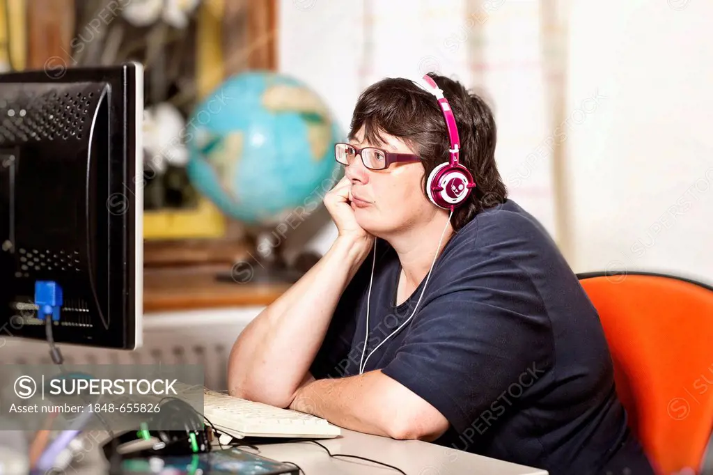 Woman wearing headphones sitting boredly in front of a computer