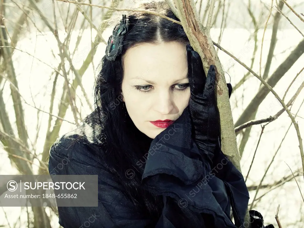 Woman, dressed in a Gothic style, Romantic-Gothic, standing in front of a bush, looking serious