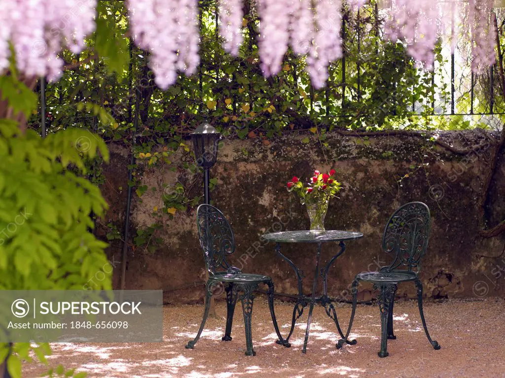Still life, round, antique cast-iron garden table and two chairs, in a romantic courtyard
