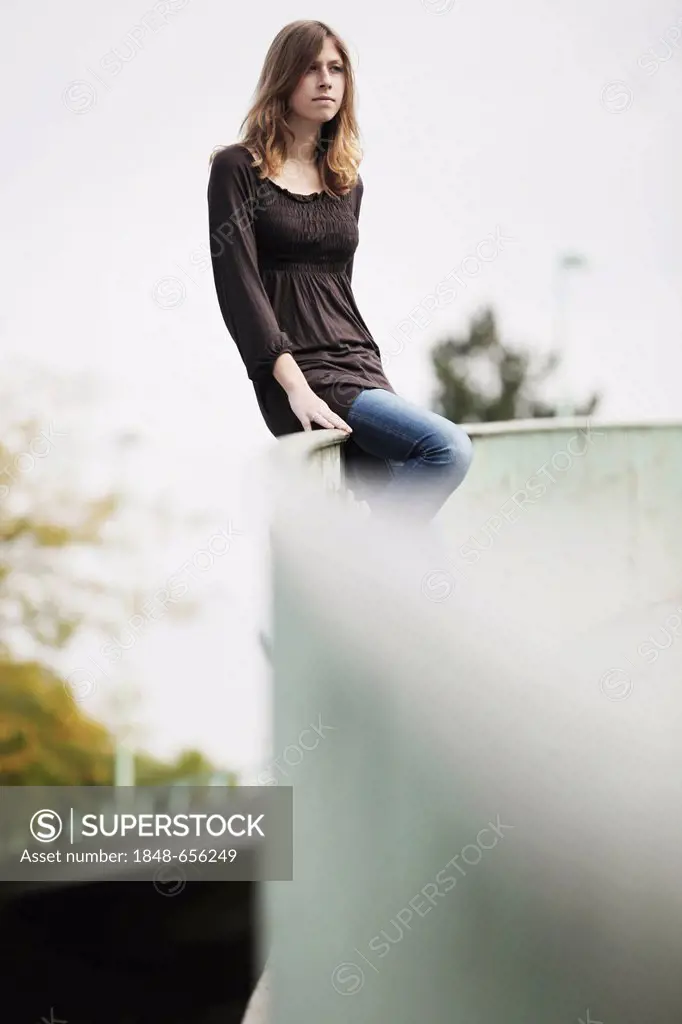 Young woman sitting on a railing, in an urban environment