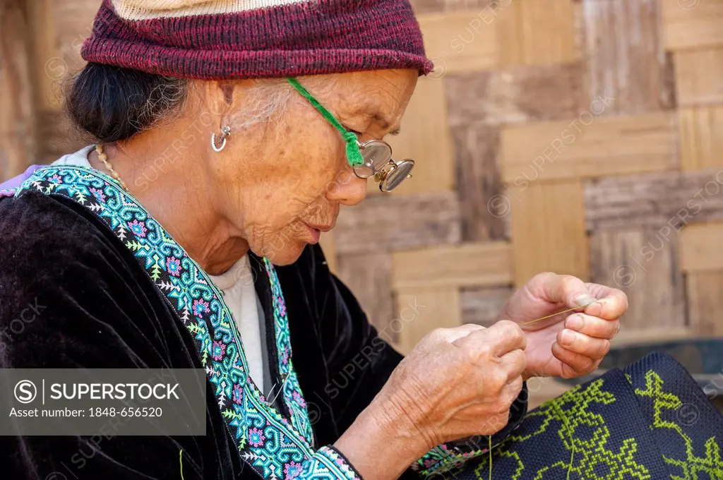 Elderly, traditionally dressed woman with glasses from the Black Hmong hill tribe, ethnic minority from East Asia, doing needlework, embroidery, North...