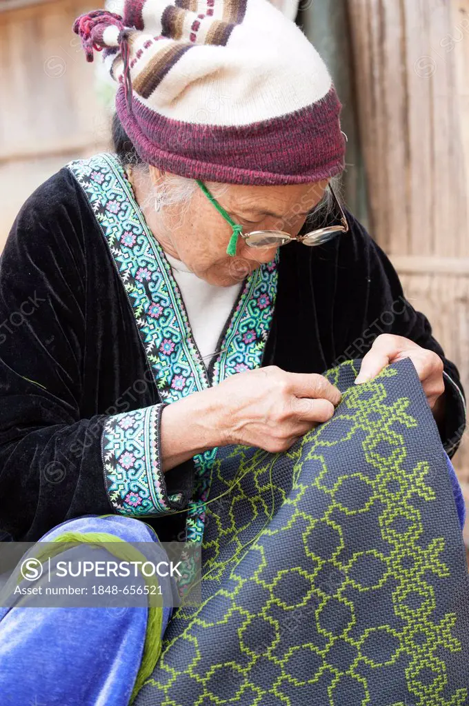 Elderly, traditionally dressed woman with glasses from the Black Hmong hill tribe, ethnic minority from East Asia, doing needlework, embroidery, North...