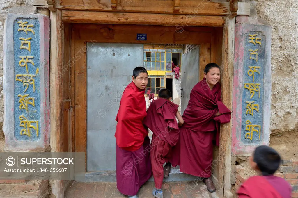 Two young novice monks, students standing in front of the entrance to a Buddhist monastery school, monastery building in the traditional architectural...