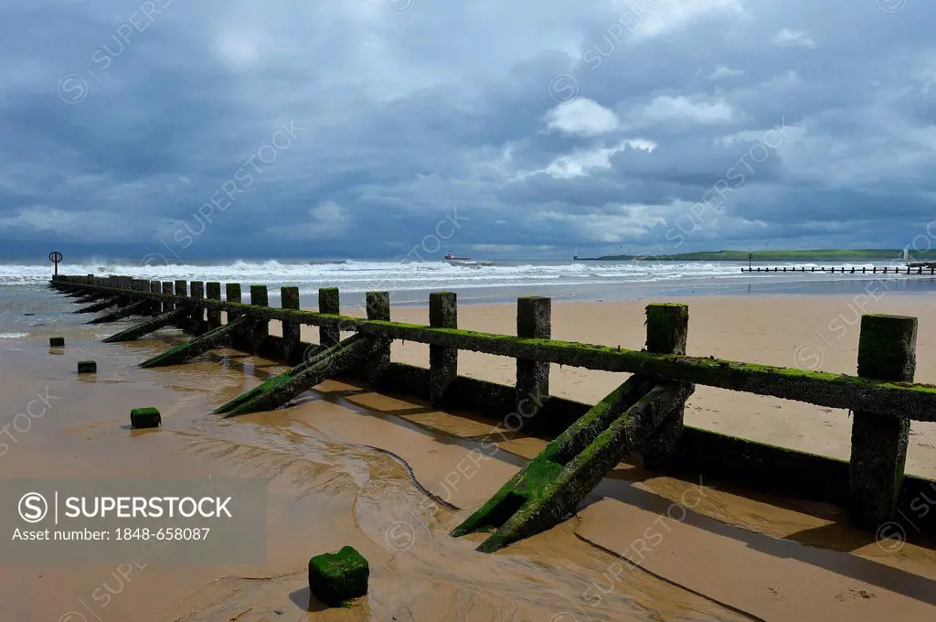 Thick, low hanging cloud cover above moss and algae covered groynes, breakwaters, at the beach, Aberdeen Scotland, United Kingdom, Europe