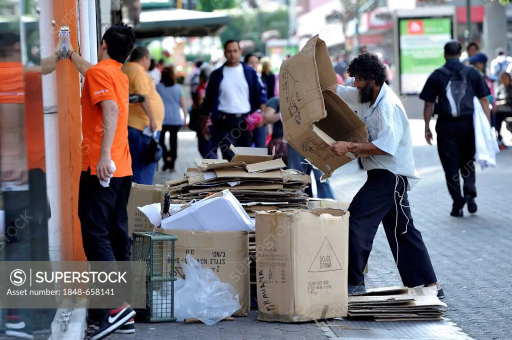 Poor man sorting recyclables or resources, cardboard boxes outside a shop, in order to sell them to a recycling plant, waste separation, pedestrian zo...