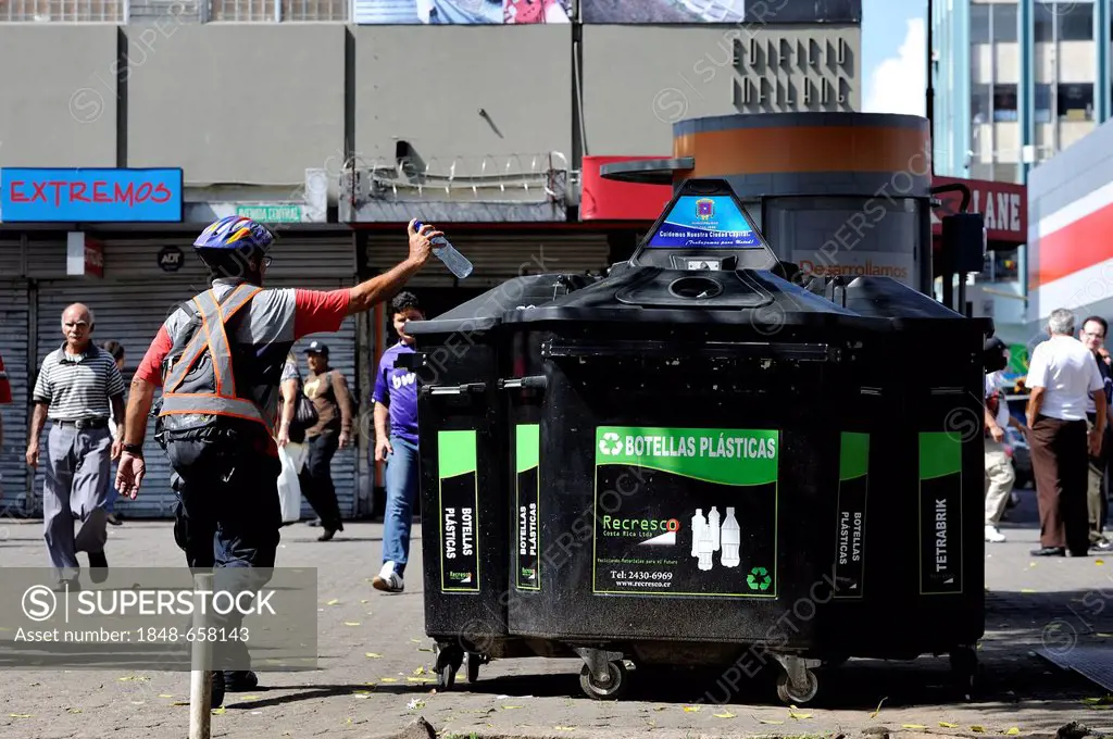 Man throwing a plastic bottle into a container for recyclables, waste separation and recycling, pedestrian zone of San José, Costa Rica, Latin America...