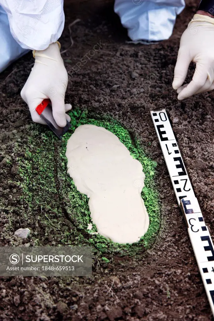 Criminal investigation department, police, forensic scientist secures a shoe print at a crime scene, making it visible with green spray paint and taki...