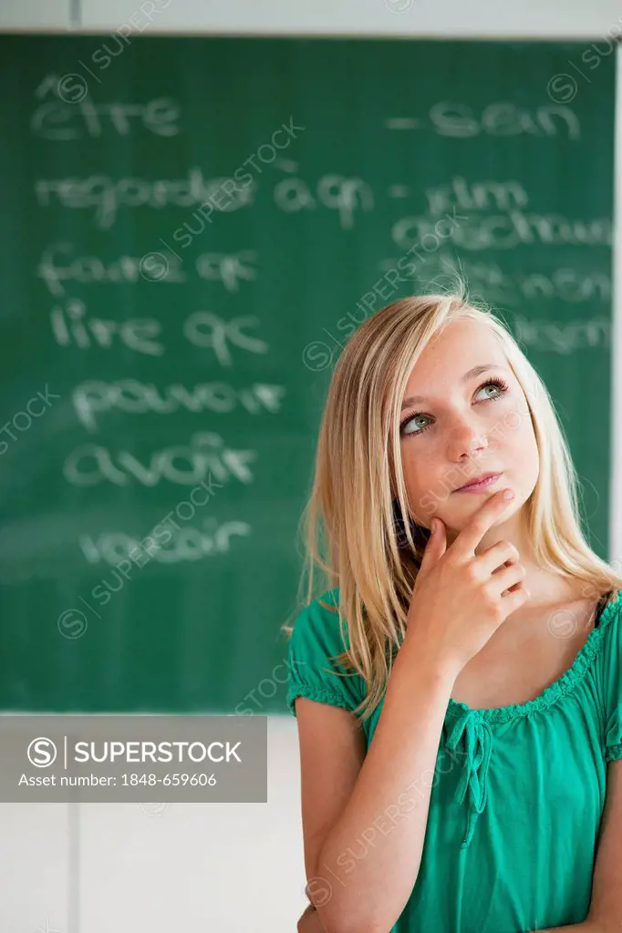 Schoolgirl standing in front of a blackboard in a classroom, looking thoughtful