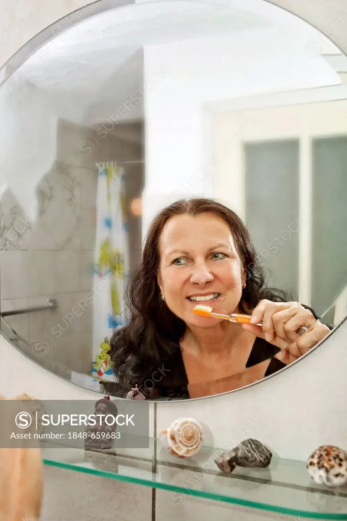 Woman brushing her teeth in front of a mirror in the bathroom