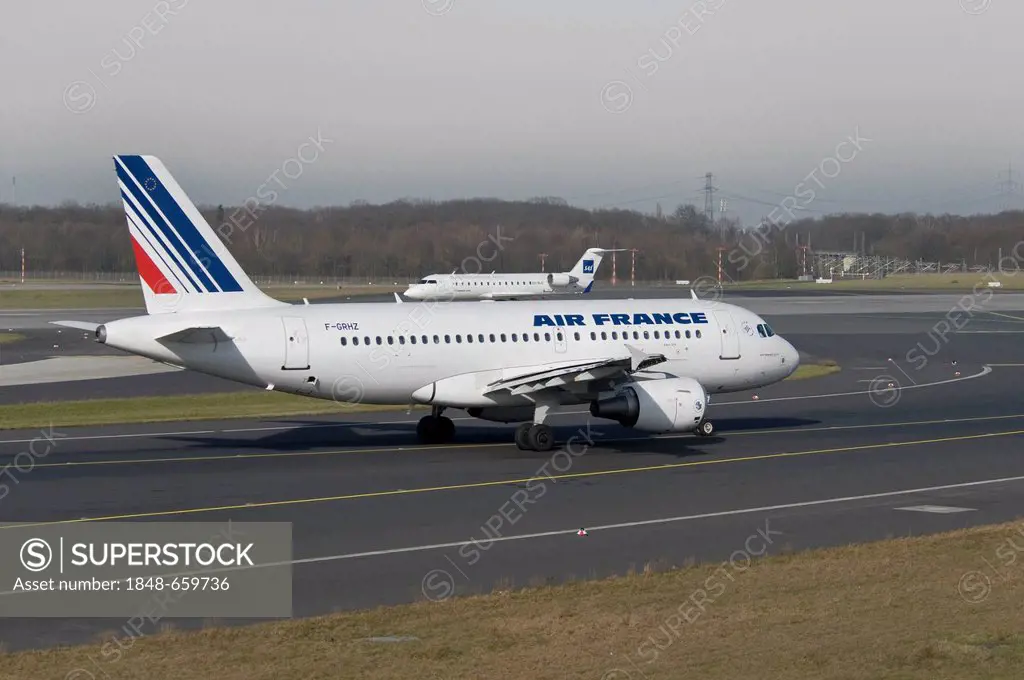Air France Airbus A319-111 passenger jet on the runway of Duesseldorf International Airport, behind, a SAS Jet taking-off, North Rhine-Westphalia, Ger...