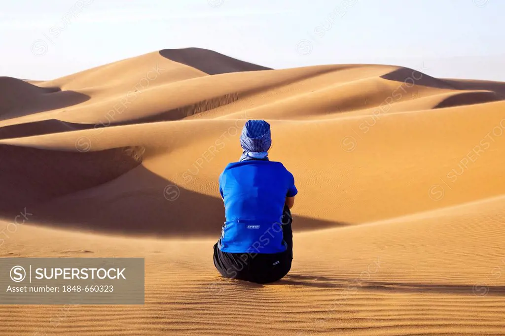 Woman sitting in the dunes, Erg Chegaga region, Sahara desert near Mhamid, Morocco, Africa