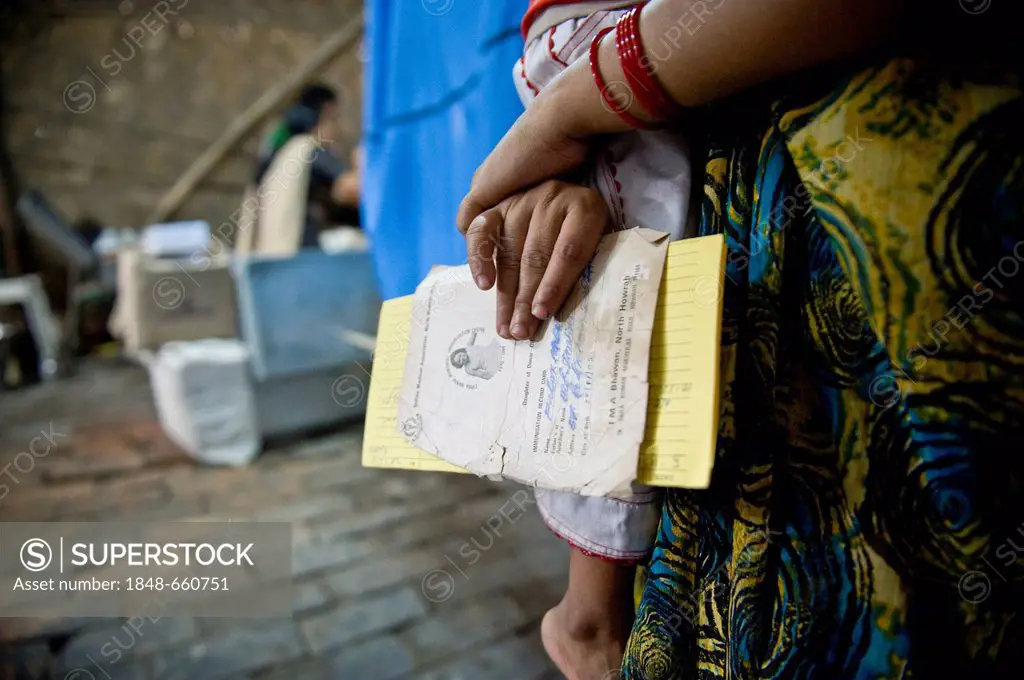 Woman waiting is holding a mother's passport, outside clinic set up in a bamboo hut by the aid organisation Aerzte fuer die Dritte Welt, German for Do...