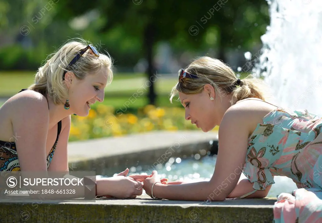 Two young women, friends, lying on a fountain, Schlosspark garden, Stuttgart, Baden-Wuerttemberg, Germany, Europe, PublicGround