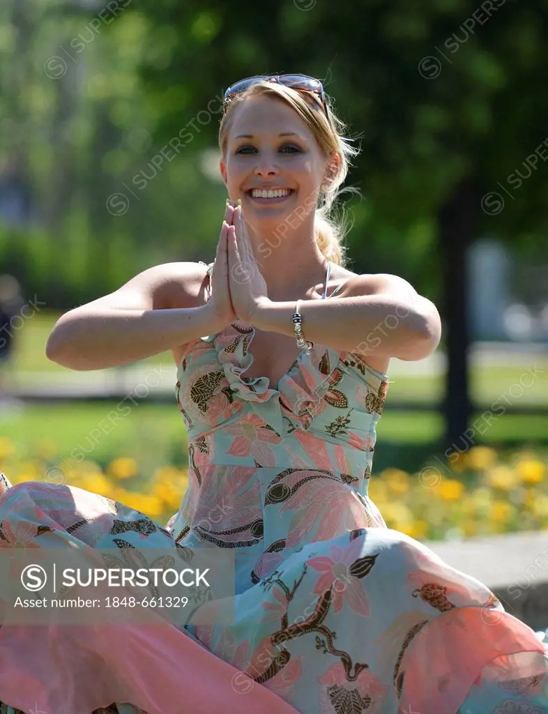 Young woman wearing a summer dress sitting in a yoga position, Schlosspark garden, Stuttgart, Baden-Wuerttemberg, Germany, Europe, PublicGround