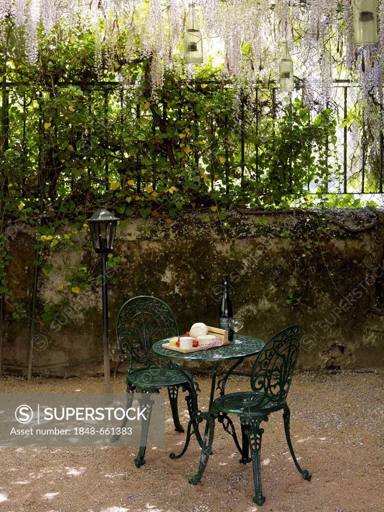 Still life, cheese buffet on an round, antique cast-iron garden table with two chairs in a romantic courtyard