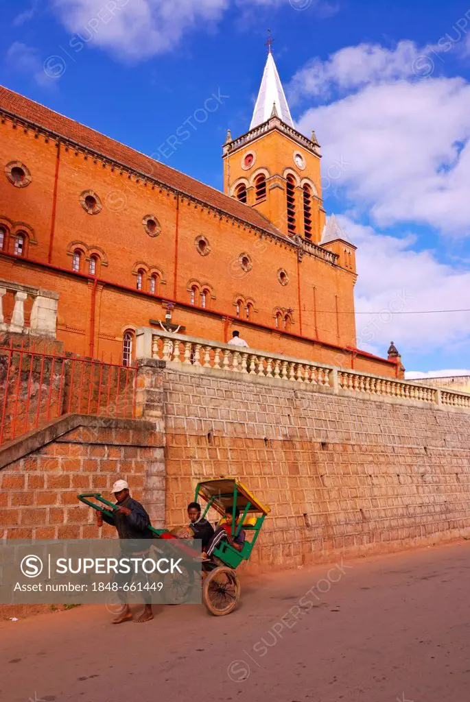 Man transporting a passenger with his rickshaw in front of a brick church in Ambositra, Madagascar, Africa