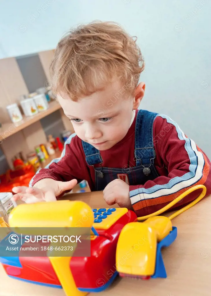 Boy, 2, playing with the cash register of a toy grocery shop