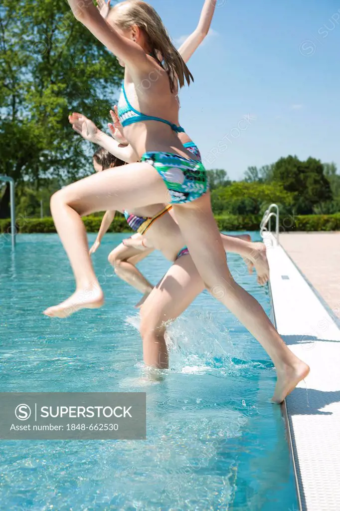 Girls jumping into the water from the edge of a public swimming pool