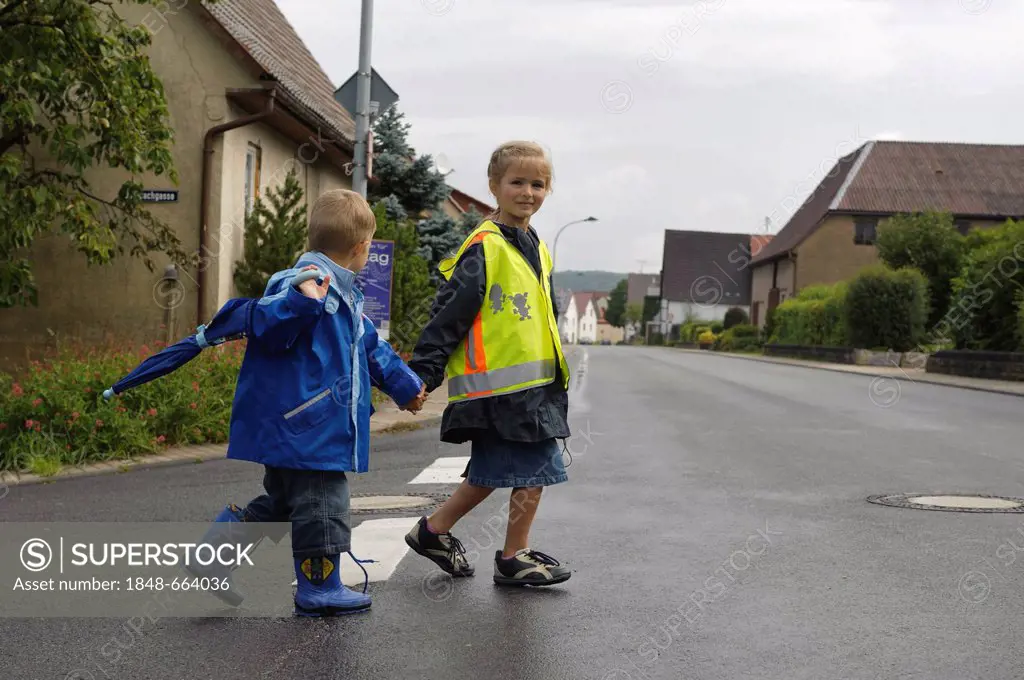 Two children, 4 and 6 years, crossing the street in the rain, Assamstadt, Baden-Wuerttemberg, Germany, Europe