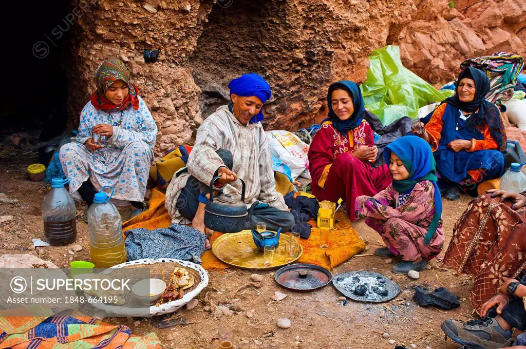 Nomadic cave-dwellers sitting in front of their cave-dwelling, a man wearing a blue turban is pouring tea into a pot on a copper tray, front left is a...
